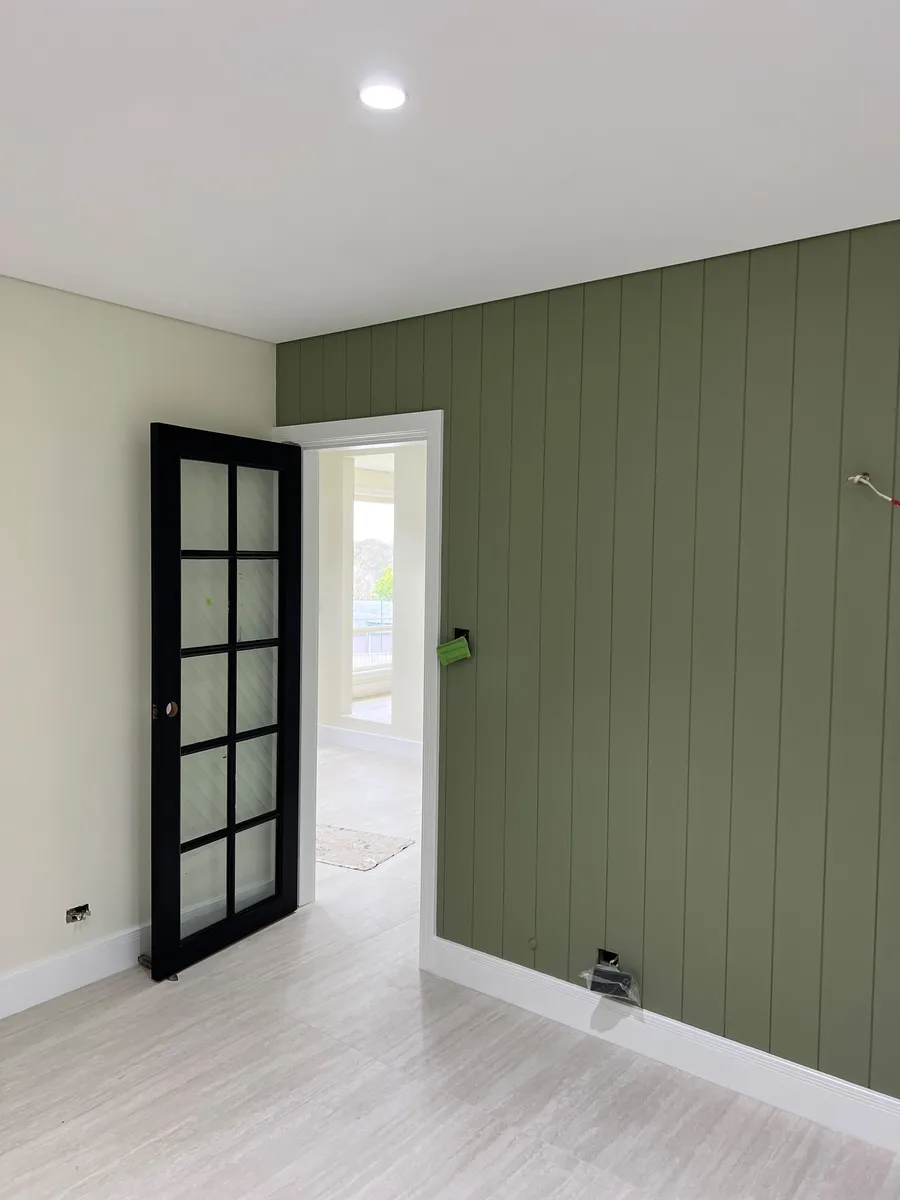 A vertical groove panelled wall painted sage green, with white skirting, architraves and ceiling