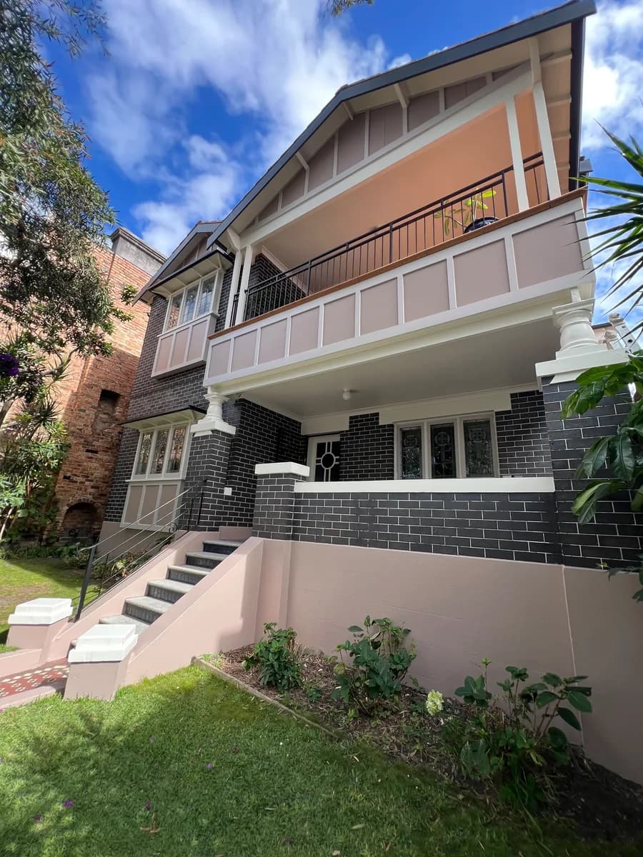 A two storey brick house with rendered panels in soft pink and cream columns, balustrade and trims