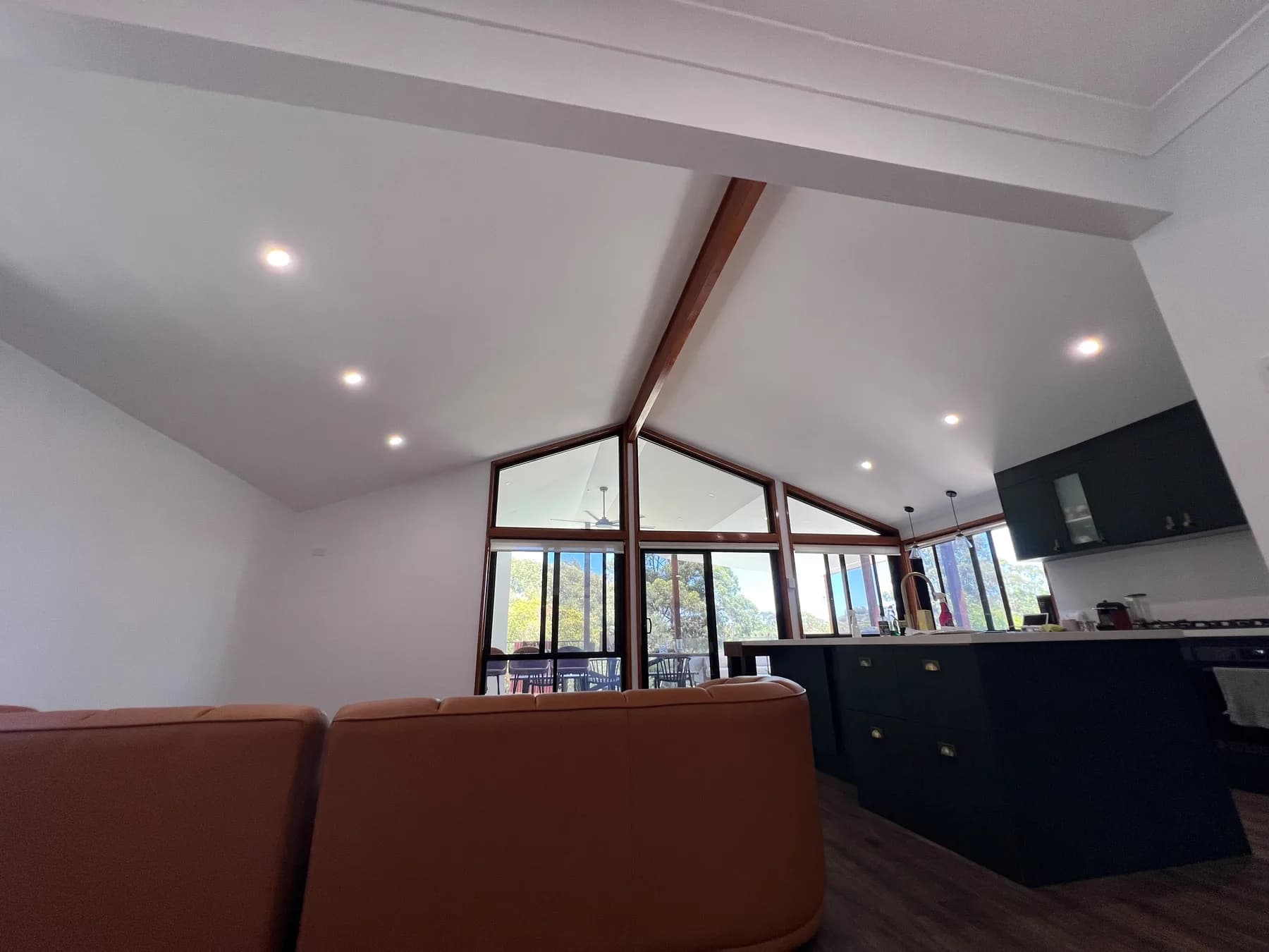 A raked white ceiling over an open plan living and kitchen space, with a timber ridge beam and timber framed gable windows