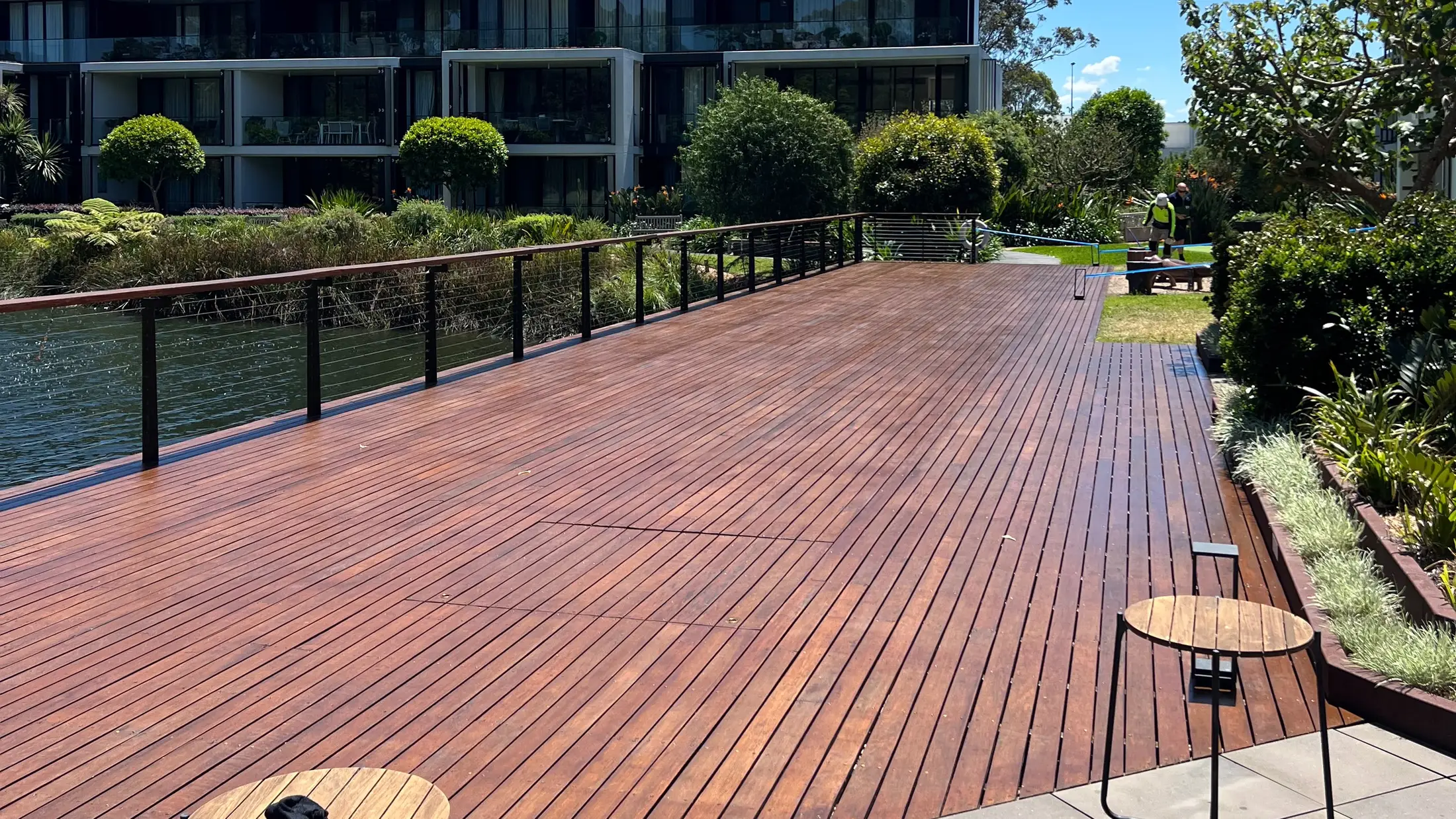 A long hardwood deck with a rich fresh finish, running beside water with landscaped garden beds alongside it