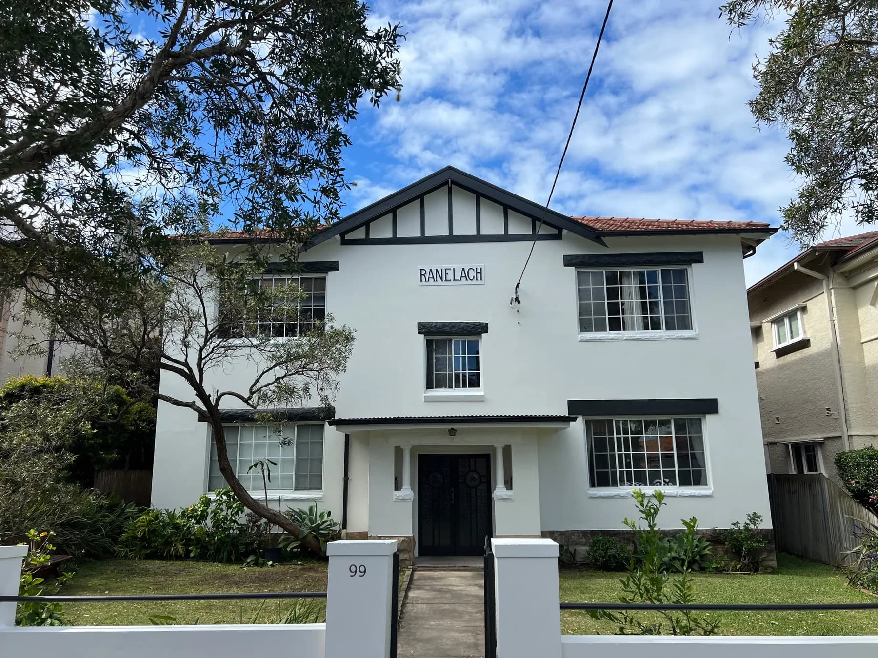 A two storey rendered exterior freshly painted white, with black trim on the gable, the window hoods and the front doors